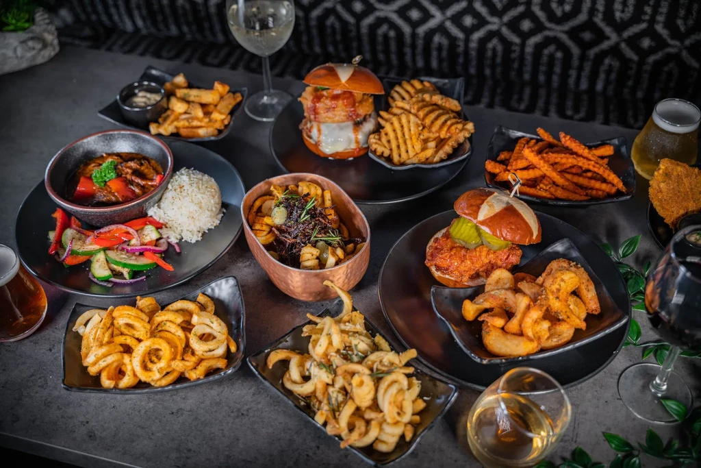 A diverse spread of burgers, fries, stew, meat, wines, and beers.
