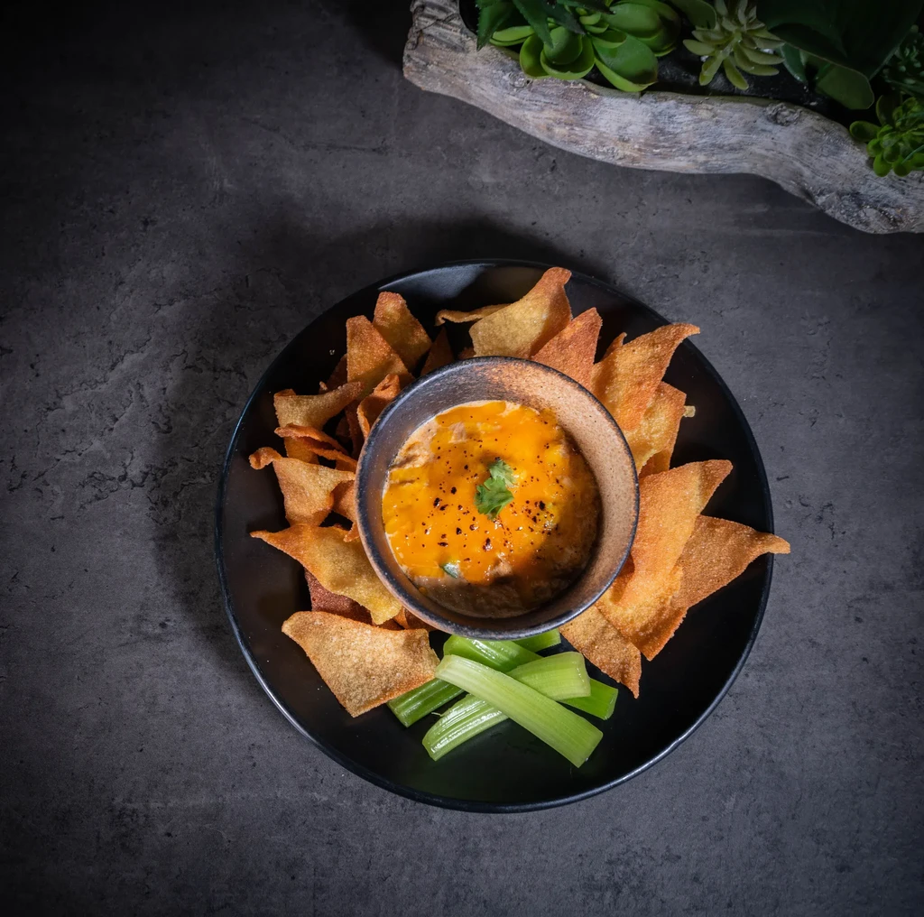 Creamy orange dip with tortilla chips and celery sticks.