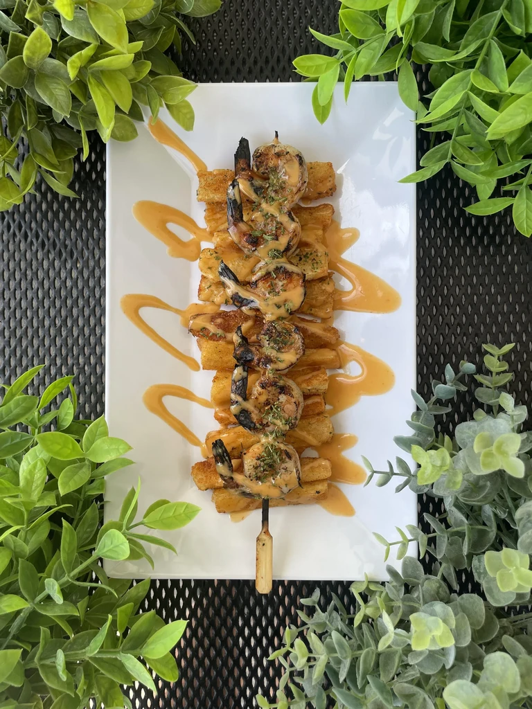Grilled shrimp skewers with herbs, bread, and orange sauce.