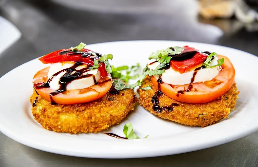 Two fried patties stacked with tomato, mozzarella, pepper, basil, balsamic glaze.