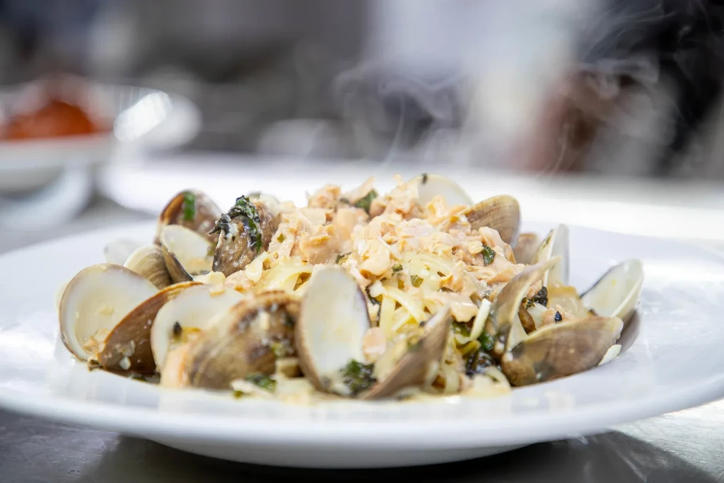 Steaming creamy pasta dish with clams, salmon, and green herbs.