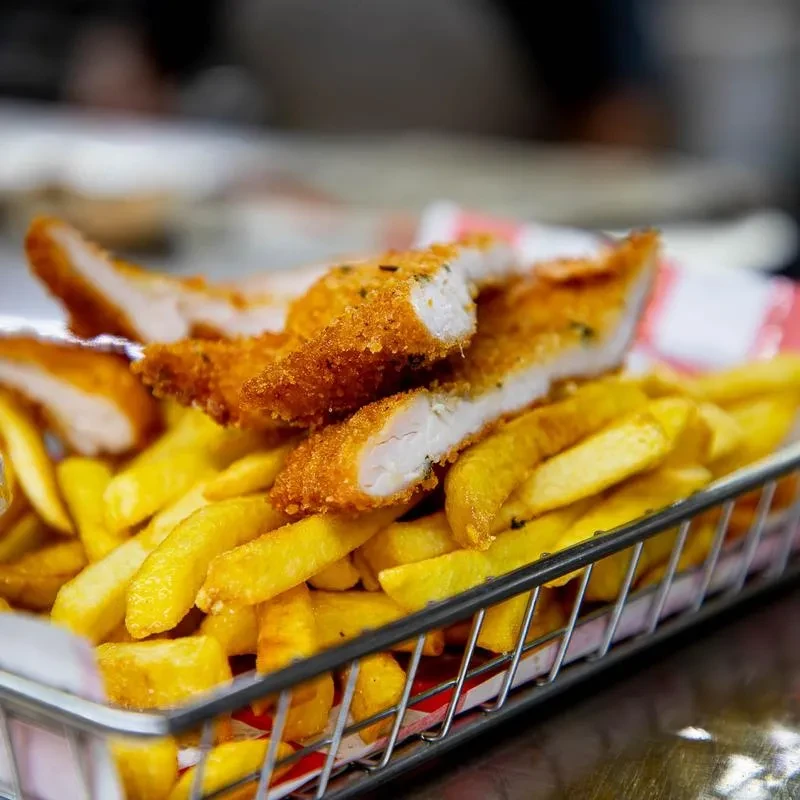 Golden-brown chicken strips and fries in a red checkered basket.