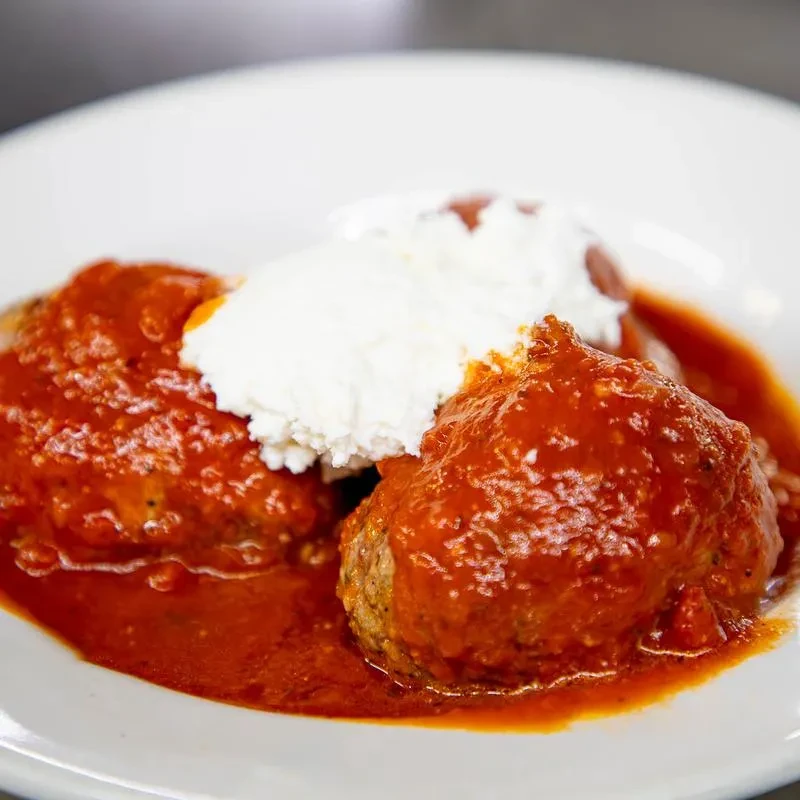 Two large meatballs with rustic tomato sauce and creamy ricotta.