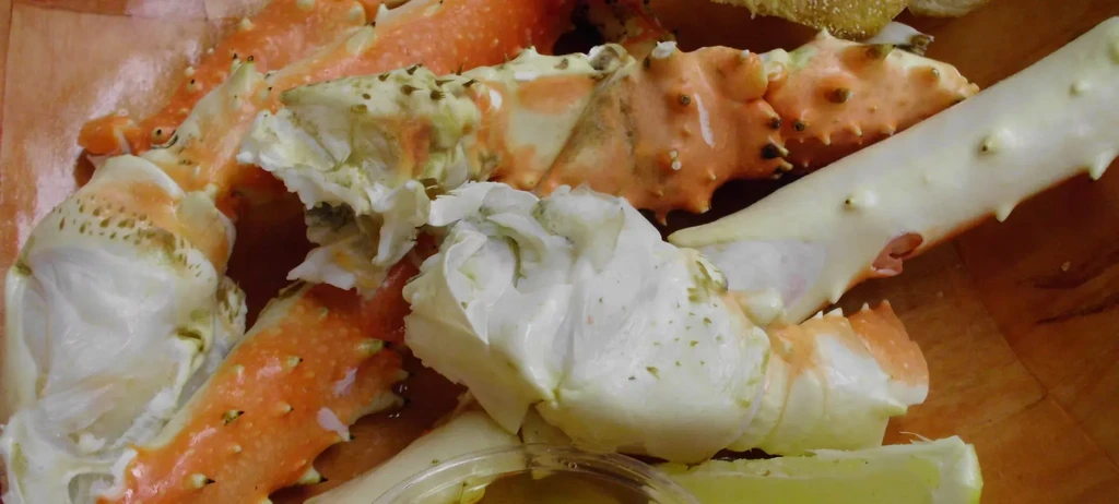 Cooked crab legs and meat in wooden bowl with sauce and lemon.