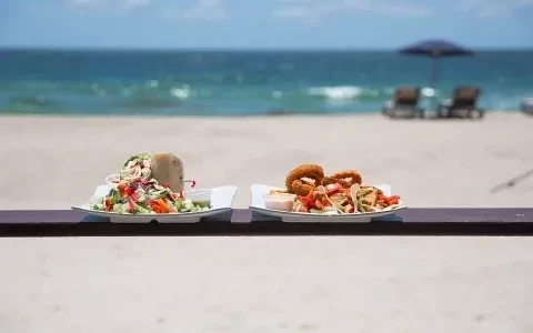 Plates with a wrap, salad, and onion rings on a beach railing.
