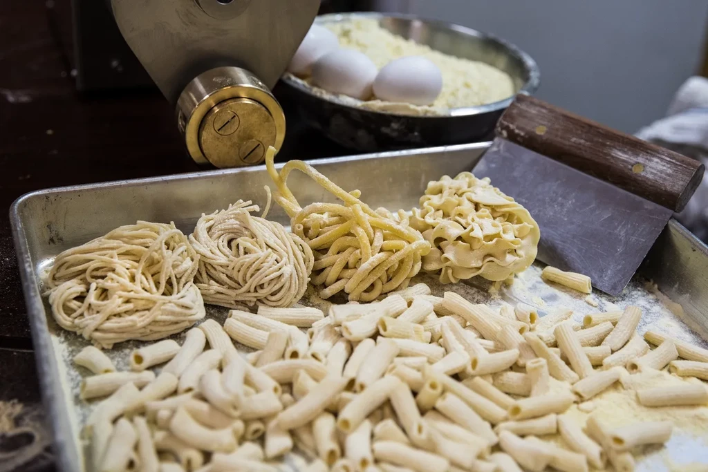 Freshly made pasta shapes on a tray with pasta machine and ingredients.