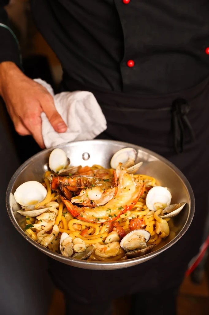 Chef holding a pan of lobster and clam pasta with herbs.