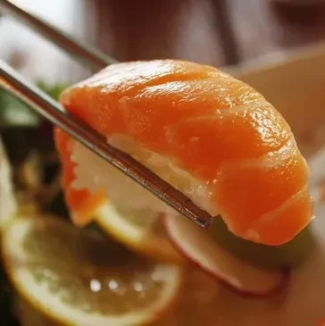 Vibrant salmon nigiri sushi held by silver chopsticks.