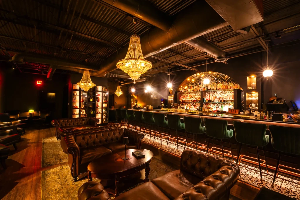 Dimly lit, elegant bar with chandeliers, Chesterfield sofas, and a grand bar.