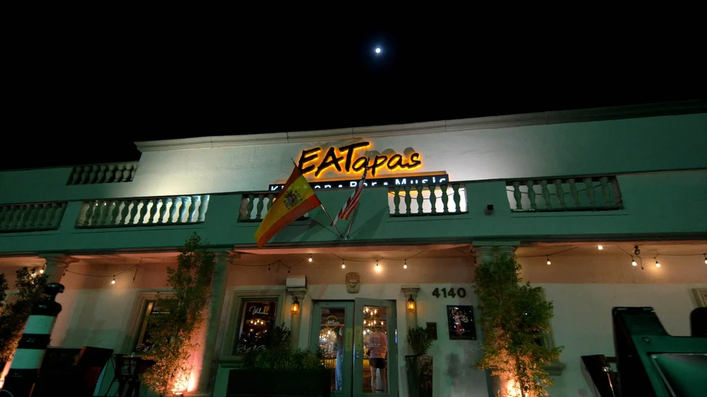EATapas restaurant exterior at night with neon sign and flags under moonlight.