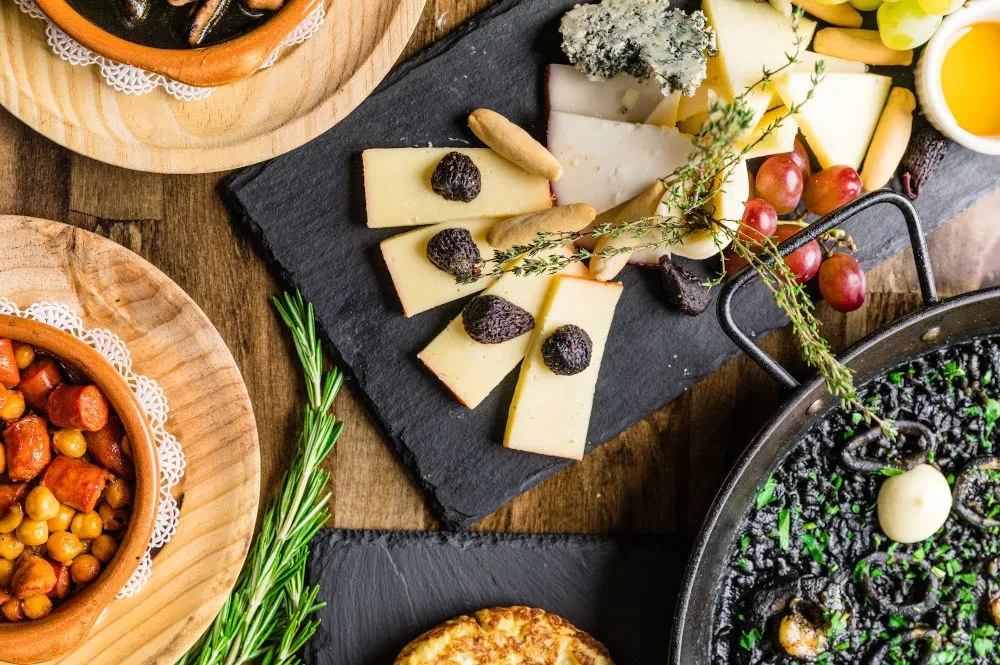 Rustic wooden table displaying a flat lay of Spanish tapas dishes.