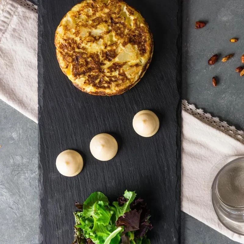Spanish tortilla, aioli, and salad on a dark slate serving board.
