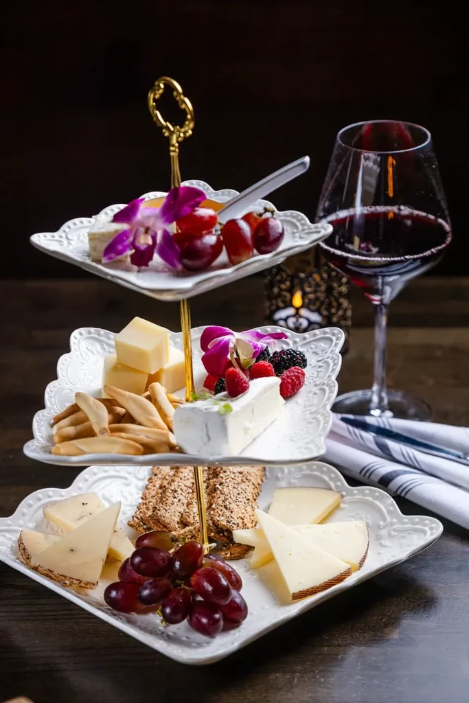 Tiered cheese and fruit platter with crackers, wine, and orchids.