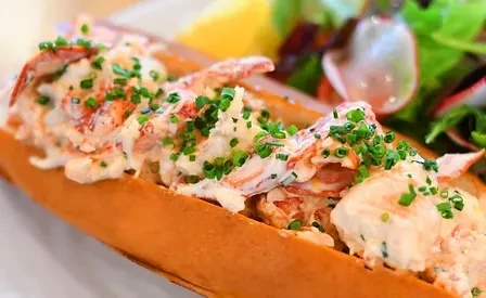 Split-top bun lobster roll with chives, side salad, lemon wedge.
