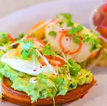 Close-up of avocado toast with two eggs, microgreens, and radishes.