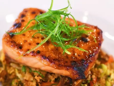 Glazed salmon with green herbs atop a grain and vegetable salad.
