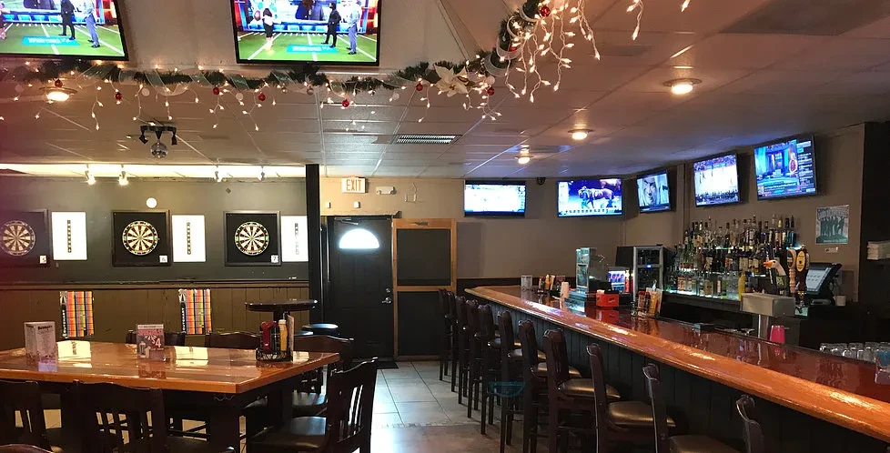 Casual bar interior featuring dartboards, sports TVs, and a stocked bar.