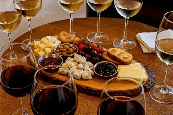 A large wooden board with cheeses, fruit, jams, and wine glasses.