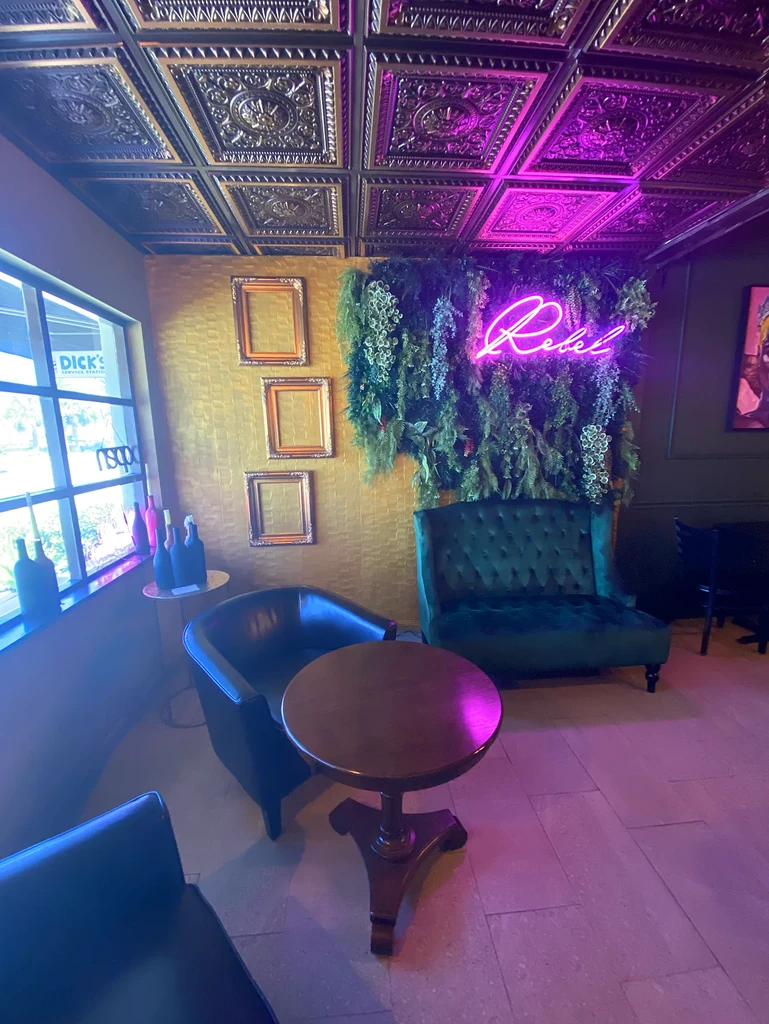 Pink-lit lounge interior with 'Rebel' neon sign and ornate details.