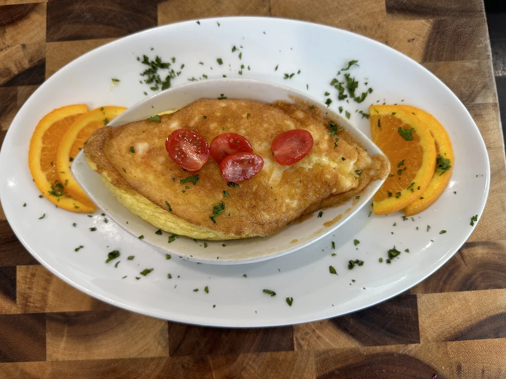 Golden-brown baked dish with tomatoes, herbs, and orange slices on wood.