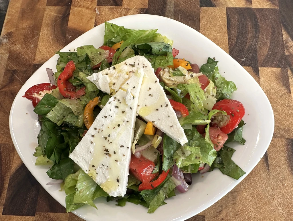 Top-down colorful Greek salad with feta and vegetables in white bowl.