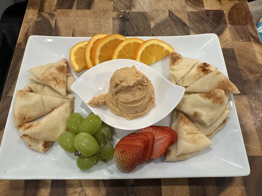 Platter of dip, pita, orange slices, green grapes, and strawberries.