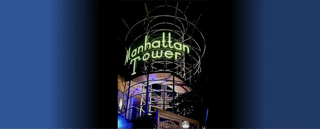 Neon "Manhattan Tower" sign on an intricate metal structure at night.