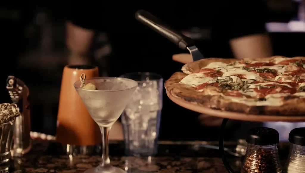 Fresh pizza, martini, and bar tools in a warm, dimly lit restaurant.