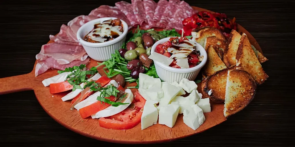 A vibrant antipasto board with meats, Caprese, bruschetta, olives, and crostini.