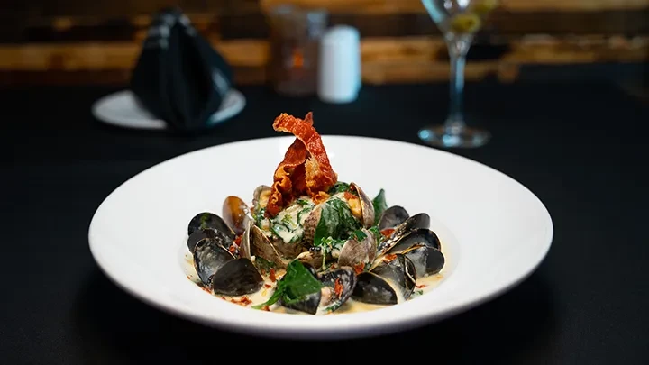Plated mussels and clams in creamy sauce with crispy strips.