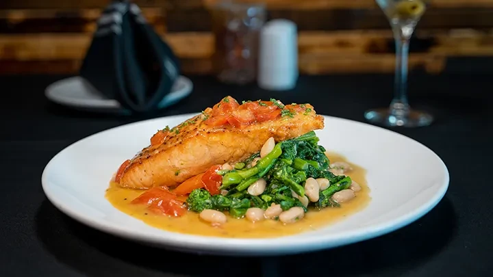 Plated salmon with tomatoes, herbs, greens, beans, and sauce.