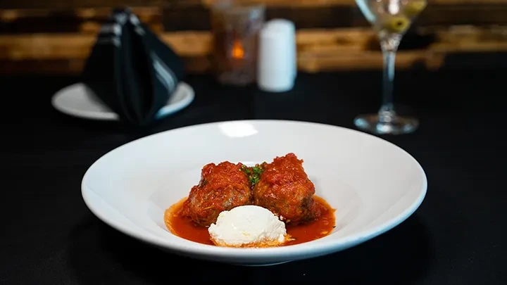 Two meatballs with marinara, ricotta, and herbs in a white bowl.