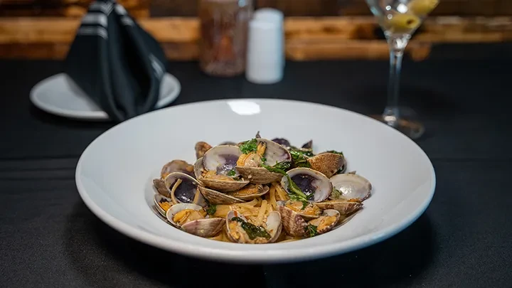 White bowl of open clams in sauce with green herbs.