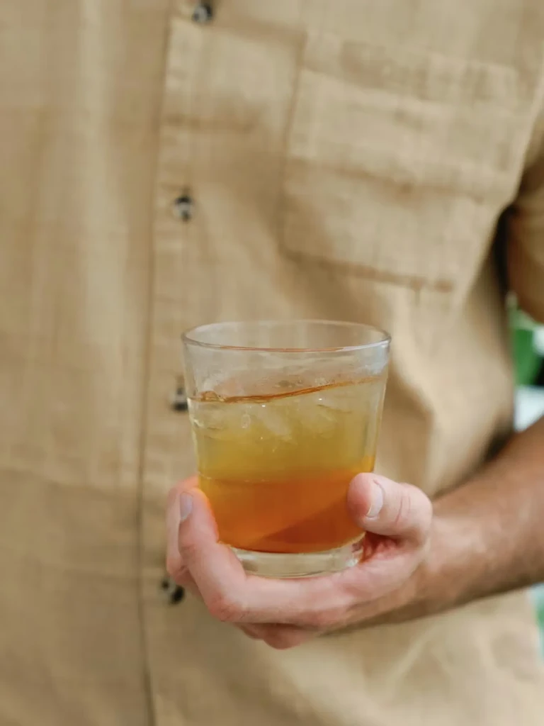 A hand holds a clear glass with a two-layered iced drink.