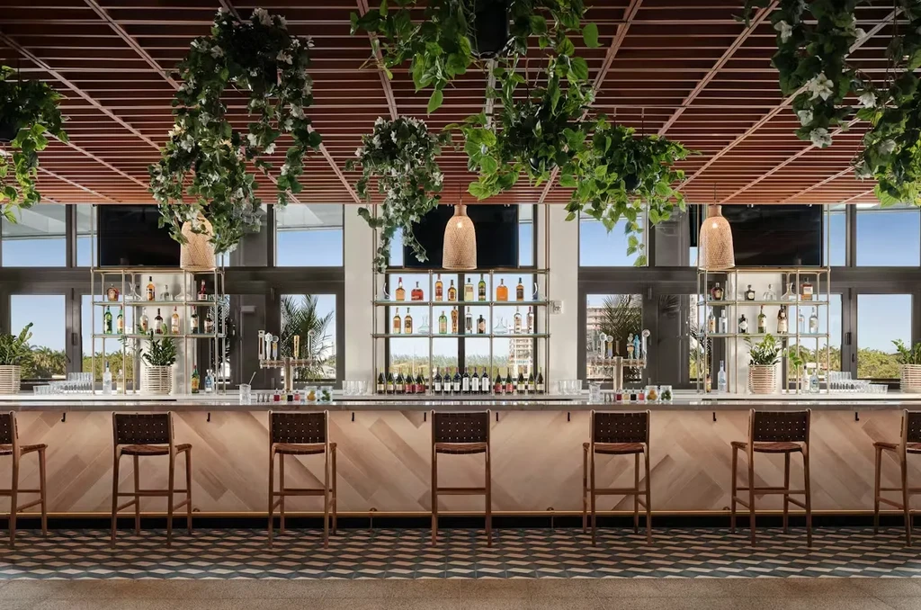 Bright modern bar area with wood counter, hanging plants, and outdoor view.