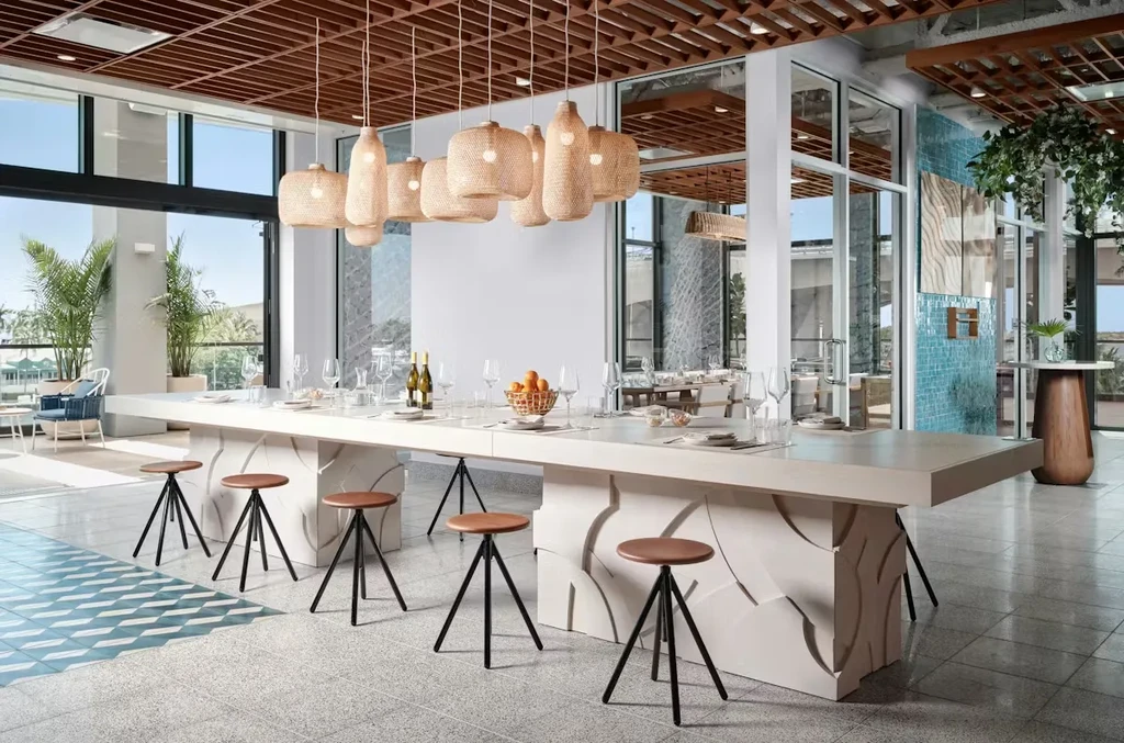 Modern restaurant interior with set communal table, wine, and tropical view.