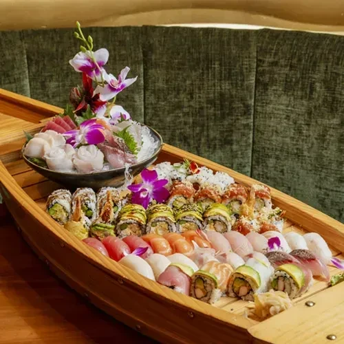 Large wooden boat overflowing with artfully presented sushi and sashimi.