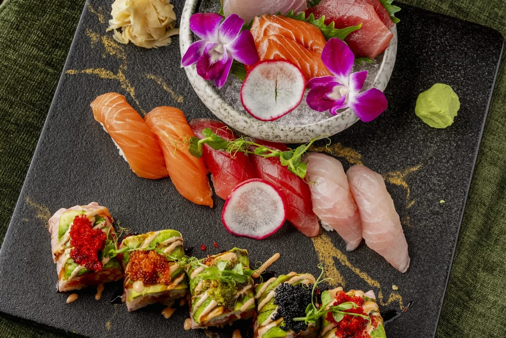 Vibrant, artfully arranged sushi, sashimi, and maki rolls on a dark platter.