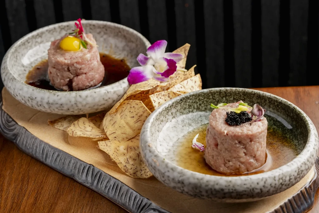 Two plated tartare dishes with caviar, egg, chips, and an orchid.