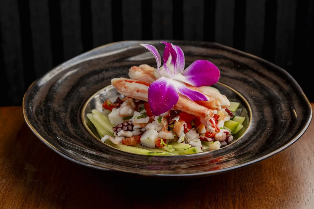 Seafood dish with fish, octopus, crab, vegetables, and orchid garnish.