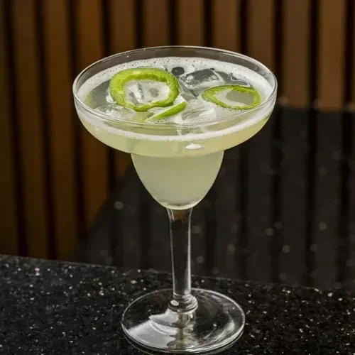Light green cocktail in a coupe glass with ice and green rings.