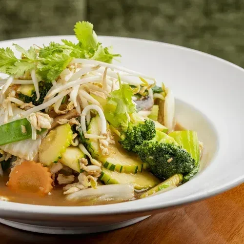 Colorful stir-fry with chicken, vegetables, and cilantro in a white bowl.