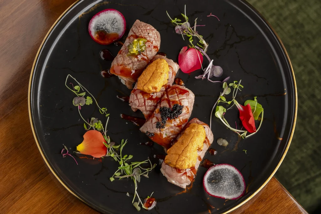 Top-down seared beef nigiri with uni and caviar, artfully garnished.