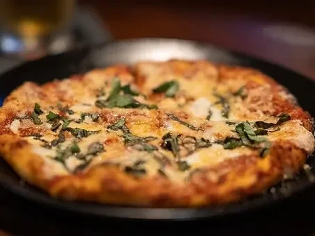 Round pizza with melted cheese, red sauce, and green basil leaves.