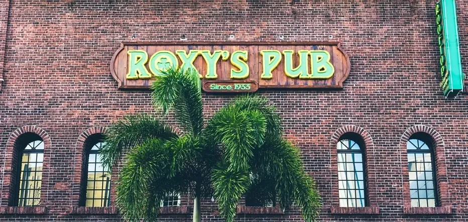 "Roxy's Pub Since 1933" sign on brick building behind a palm tree.