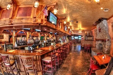 Rustic bar interior with wooden bar, beer taps, TVs, and fireplace.