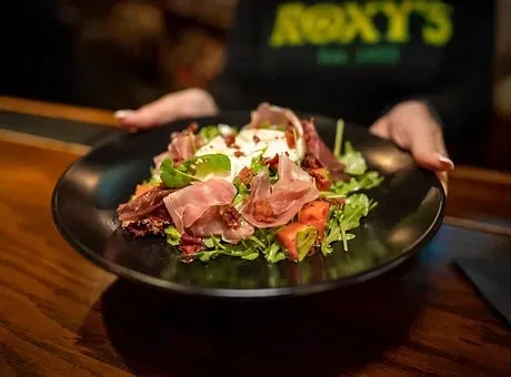 Arugula, prosciutto, cheese, and tomato salad on a black plate.