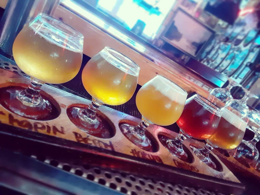 Five distinct drinks in stemmed glasses on a wooden paddle.