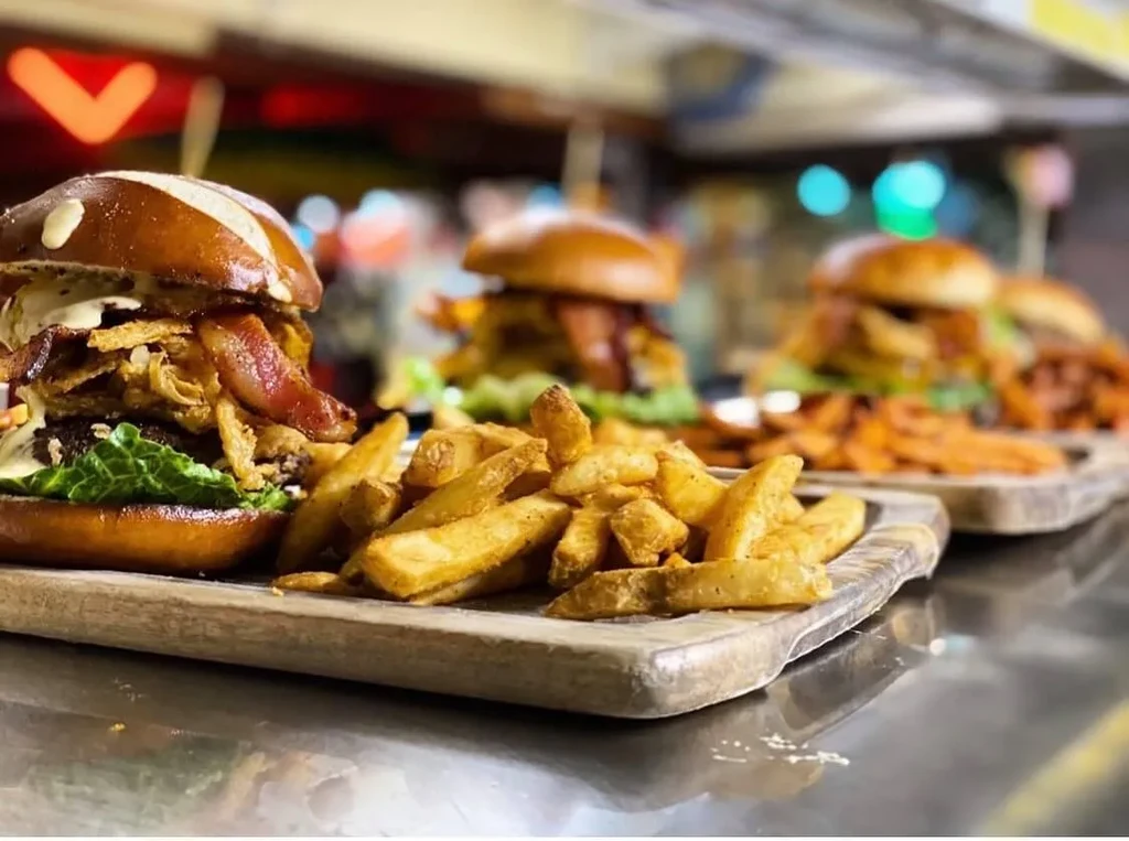 Three gourmet burgers, pretzel bun, fries on wooden boards in a restaurant.