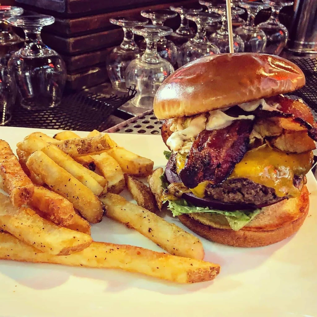 Gourmet burger with melted cheddar and bacon, next to seasoned fries.